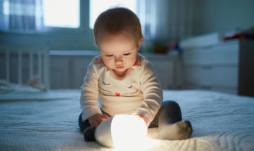 Adorable baby girl playing with bedside lamp in nursery