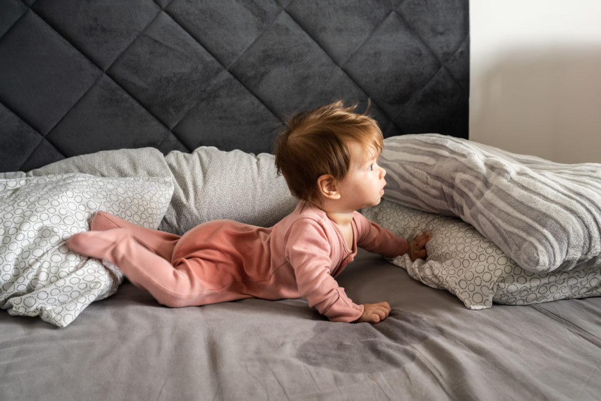 Small caucasian baby lying down on the belly on the bed with wet urine stain on the sheet and clothes looking to the side Bedwetting child pee on the bed