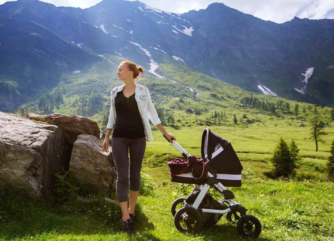 Maman en balade avec une poussette tout-terrain en pleine nature dans un paysage de montagne