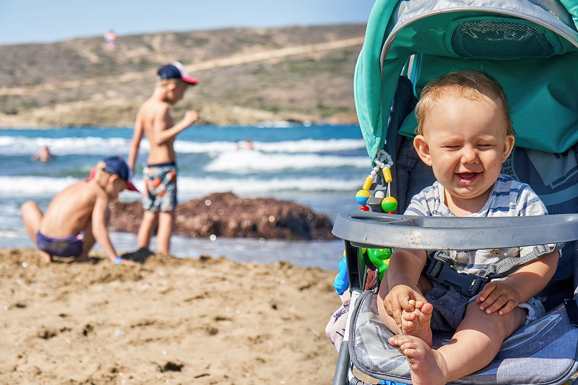 Bébé installé dans une poussette pour la plage, équipée d’accessoires pour le confort et la protection solaire.