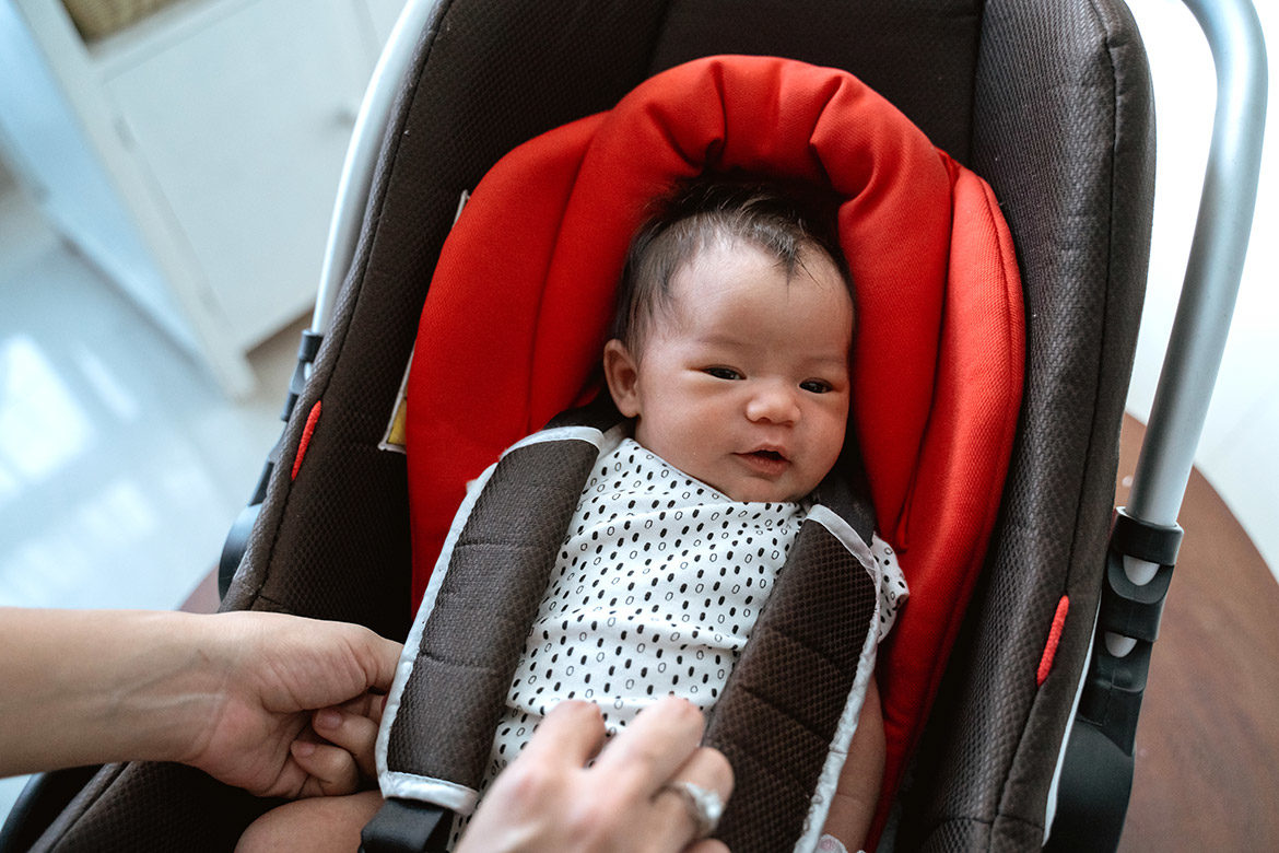 Bébé installé dans une coque de siège auto avec un harnais ajusté par les mains de sa maman