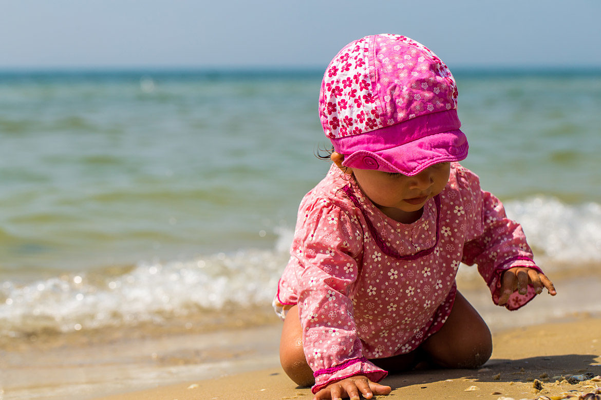 Bébé rampant sur le sable avec un chapeau pour le soleil et des vêtements anti-uv.
