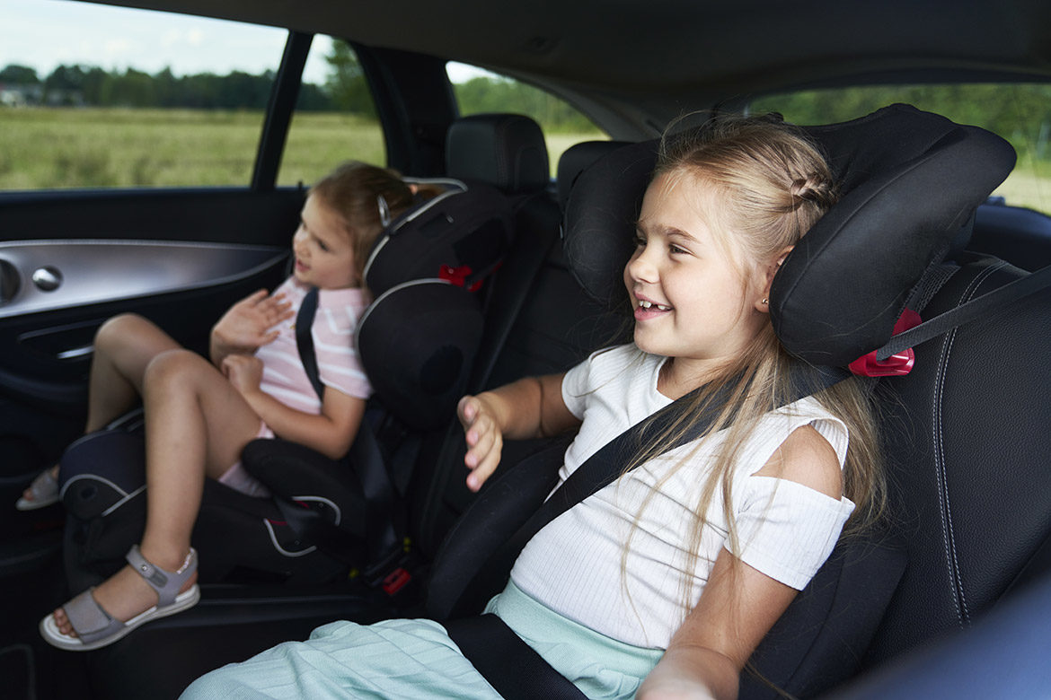 Deux petites filles à l’arrière d’une voiture, installées dans des rehausseurs avec dossier et ceinture de sécurité