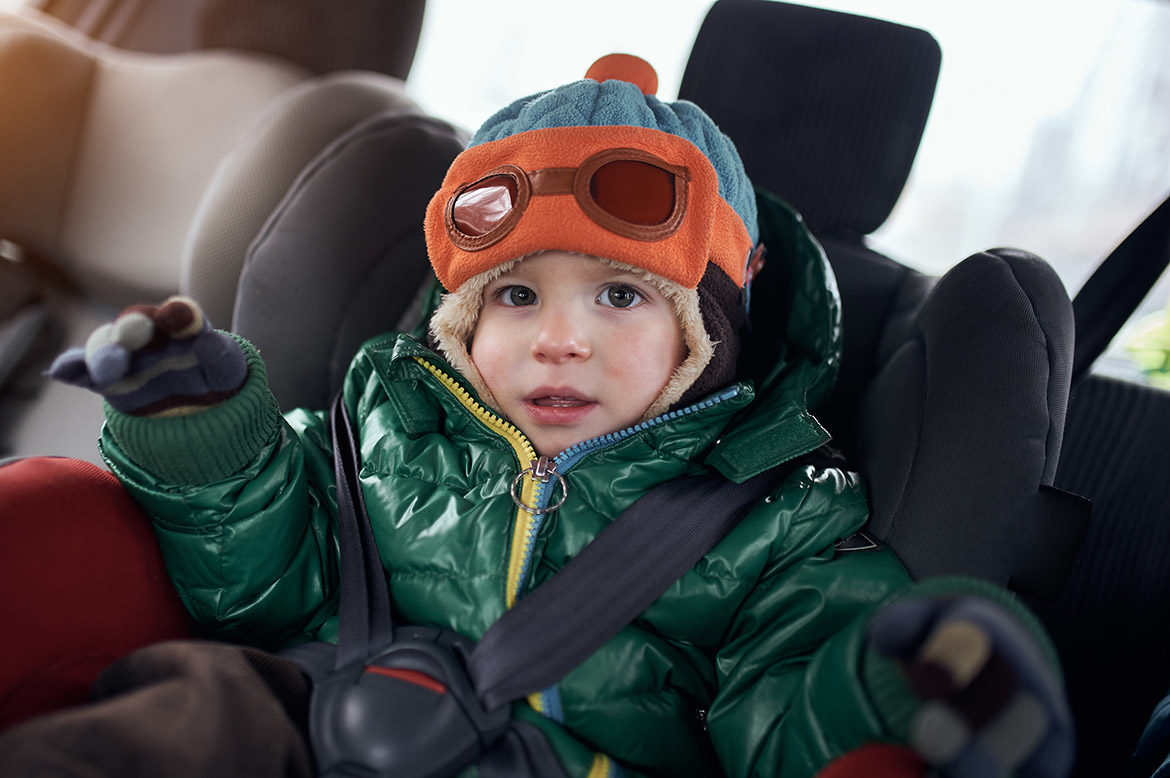 Petit garçon installé dans un siège auto avec un manteau épais d’hiver, un bonnet et des gants