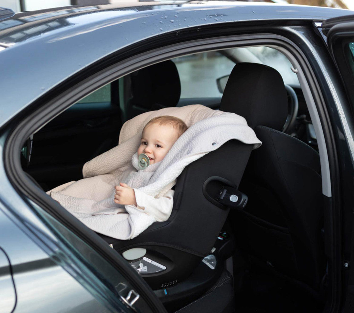 Bébé installé dans un siège auto avec un poncho par-dessus le harnais pour être protégé du froid