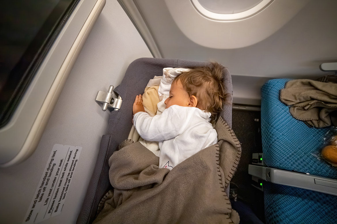 Vue du dessus d’un bébé endormi dans un berceau, installé dans un avion devant les places assises.