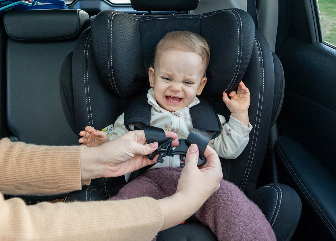 Bébé qui pleure en voiture pendant que sa maman ajuste le harnais du siège auto