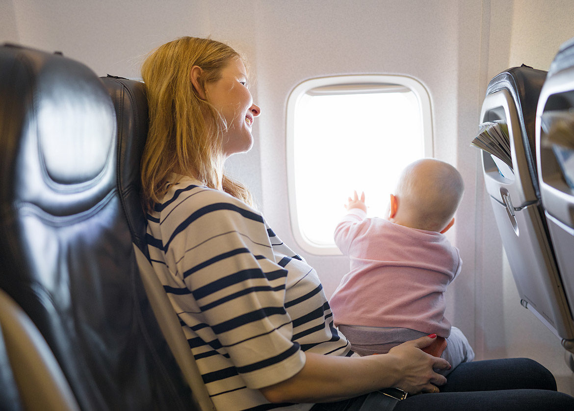 Maman avec bébé sur ses genoux dans un avion, attachés par une ceinture de sécurité et regardant par le hublot