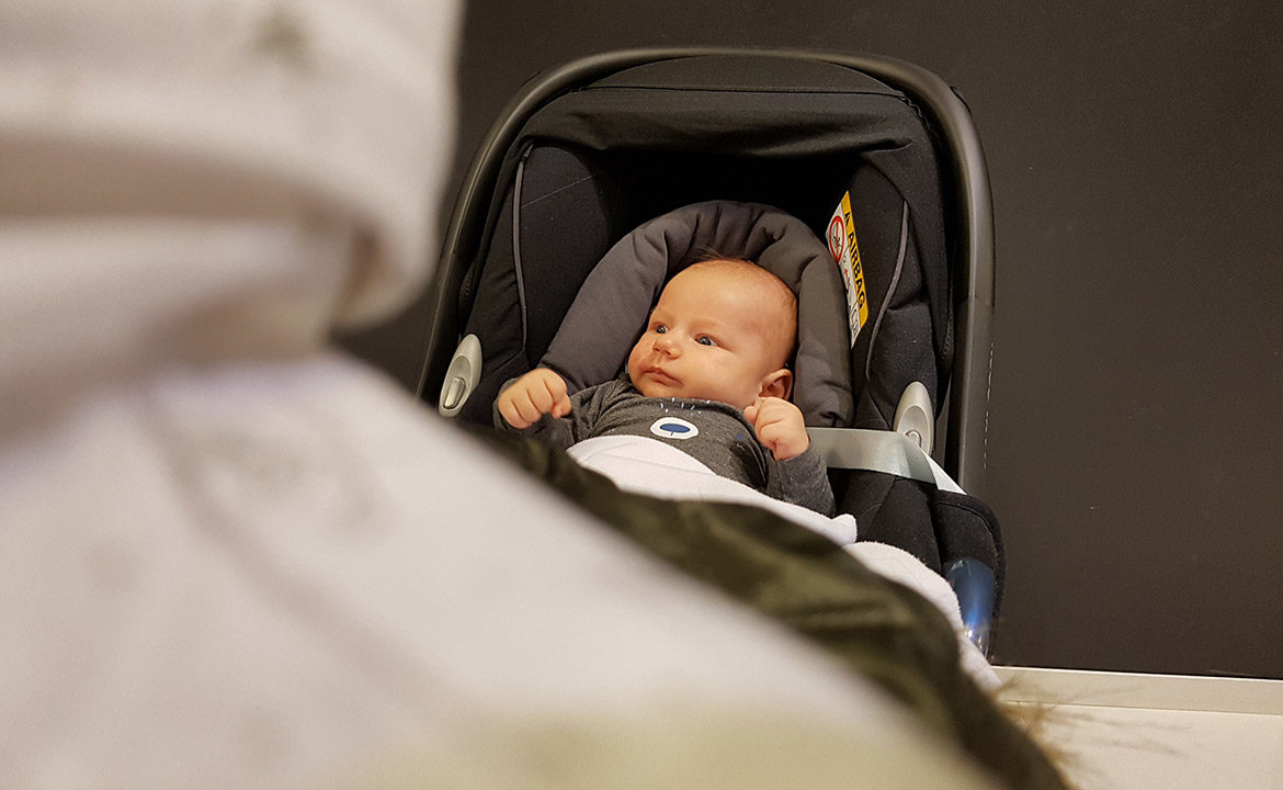 Bébé installé dans un cosy hors de la voiture, harnais détaché pendant une pause sur la route